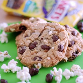 Cookies with raisinets and popcorn, on a green paper. Raisinet wrappers in the background and popcorn and loose raisinets in the foreground.