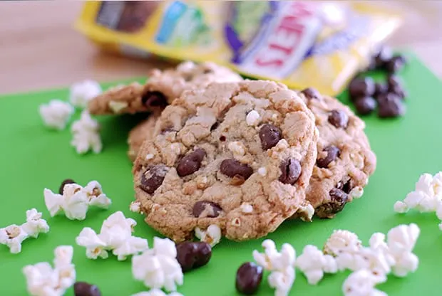 Cookies with raisinets and popcorn, on a green paper. Raisinet wrappers in the background and popcorn and loose raisinets in the foreground.