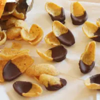 Frito corn chips pouring out of a bag on a sheet of parchment paper. Each chip has been half dipped in chocolate.