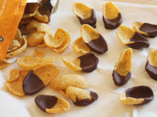 Frito corn chips pouring out of a bag on a sheet of parchment paper. Each chip has been half dipped in chocolate.
