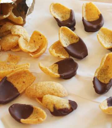 Frito corn chips pouring out of a bag on a sheet of parchment paper. Each chip has been half dipped in chocolate.