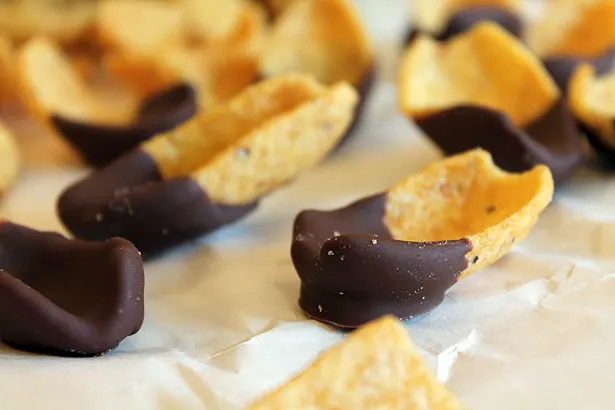 Large "scoops" style frito corn chips half dipped in milk chocolate on a sheet of parchment paper.