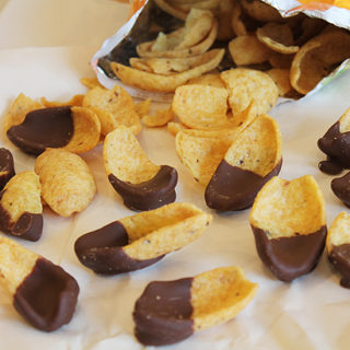 Frito corn chips on a piece of parchment paper as they pour out of the bag. Each chip is dipped halfway in milk chocolate.