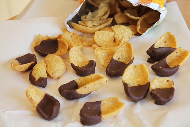 Frito corn chips on a piece of parchment paper as they pour out of the bag. Each chip is dipped halfway in milk chocolate.