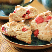 Fresh strawberry triangle-shaped scones on a blue ceramic plate. A teapot sits in the background.