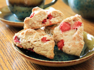 Fresh strawberry triangle-shaped scones on a blue ceramic plate. A teapot sits in the background.