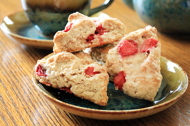 Fresh strawberry triangle-shaped scones on a blue ceramic plate. A teapot sits in the background.