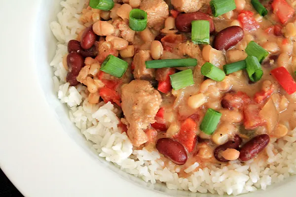 White chicken chili in a bowl, over rice. The chili includes chicken breast, kidney beans, navy beans and white shoepeg corn.