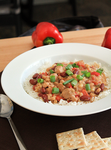 White chicken chili in a bowl, surrounded by saltine crackers and red peppers. The chili is served over white rice.