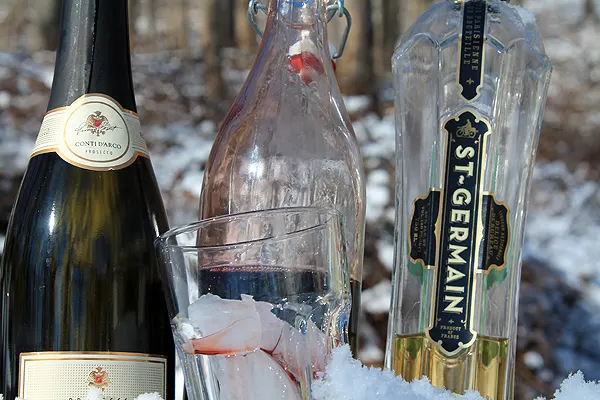 Classic St. Germain Cocktail made with prosecco, elderflower cordial and homemade grenadine. All three bottles sit in the snow.
