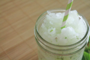 Lime, mint, sugar and ice blended drink in a glass jar. The drink also has a green striped straw.
