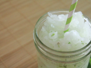 Lime, mint, sugar and ice blended drink in a glass jar. The drink also has a green striped straw.