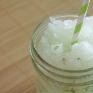 Lime, mint, sugar and ice blended drink in a glass jar. The drink also has a green striped straw.