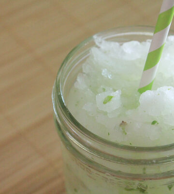 Lime, mint, sugar and ice blended drink in a glass jar. The drink also has a green striped straw.