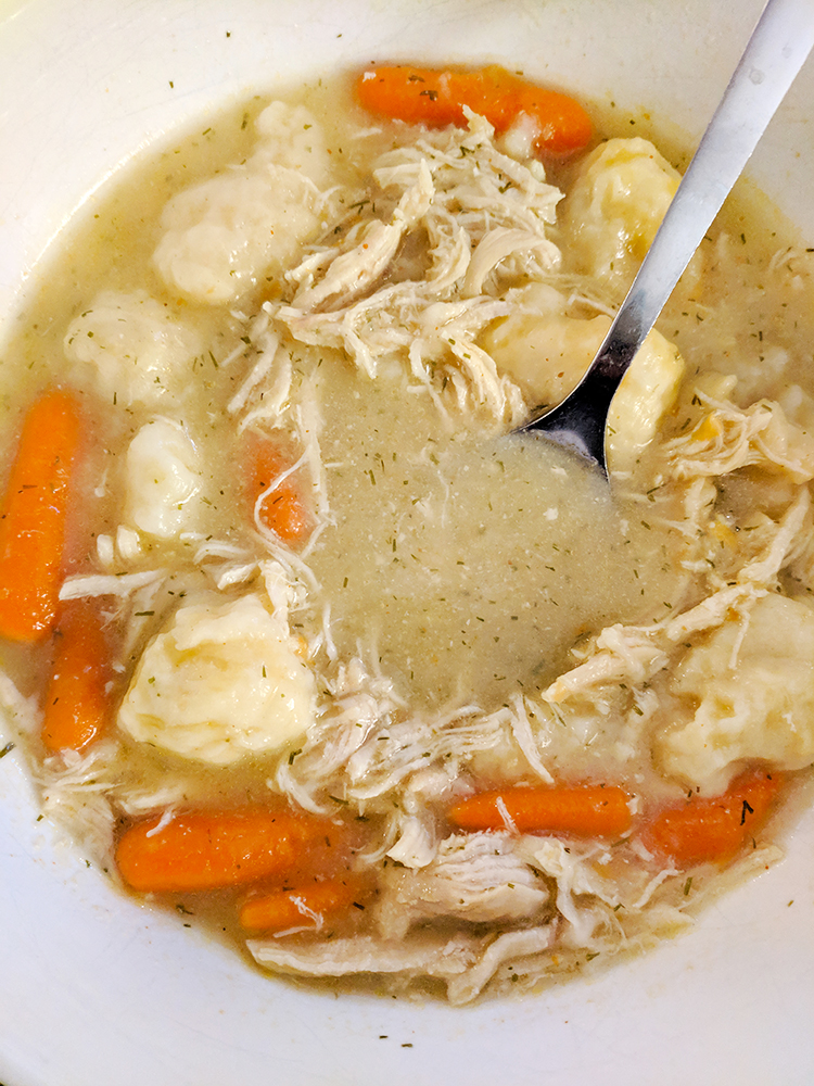Chicken, dumplings and carrots with dill in a white bowl.